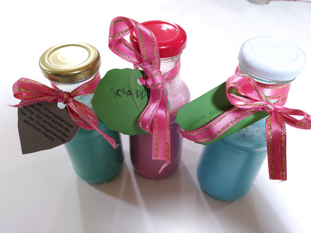 drei Glasflaschen mit selbstgemachtem Duschgel in den Farben türkis hellblau und pink
