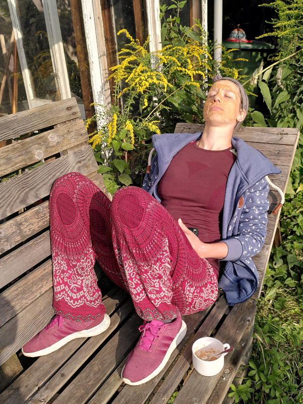 Frau mit Möhrenmaske im Gesicht entspannt auf einer Holzbank im Garten