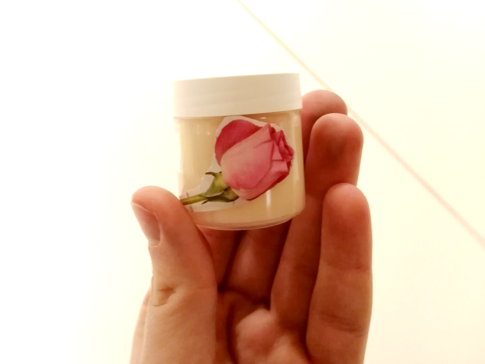 Kinderhand hält mit Rosenbild dekoriertes Gefäß befüllt mit selbst gemachten Lippenbalsam